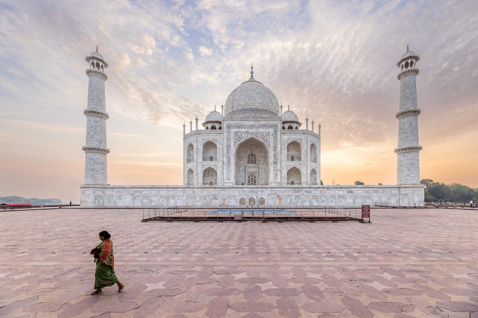 The Taj Mahal at dawn. A lady in a sari walks by the Taj just before sunrise